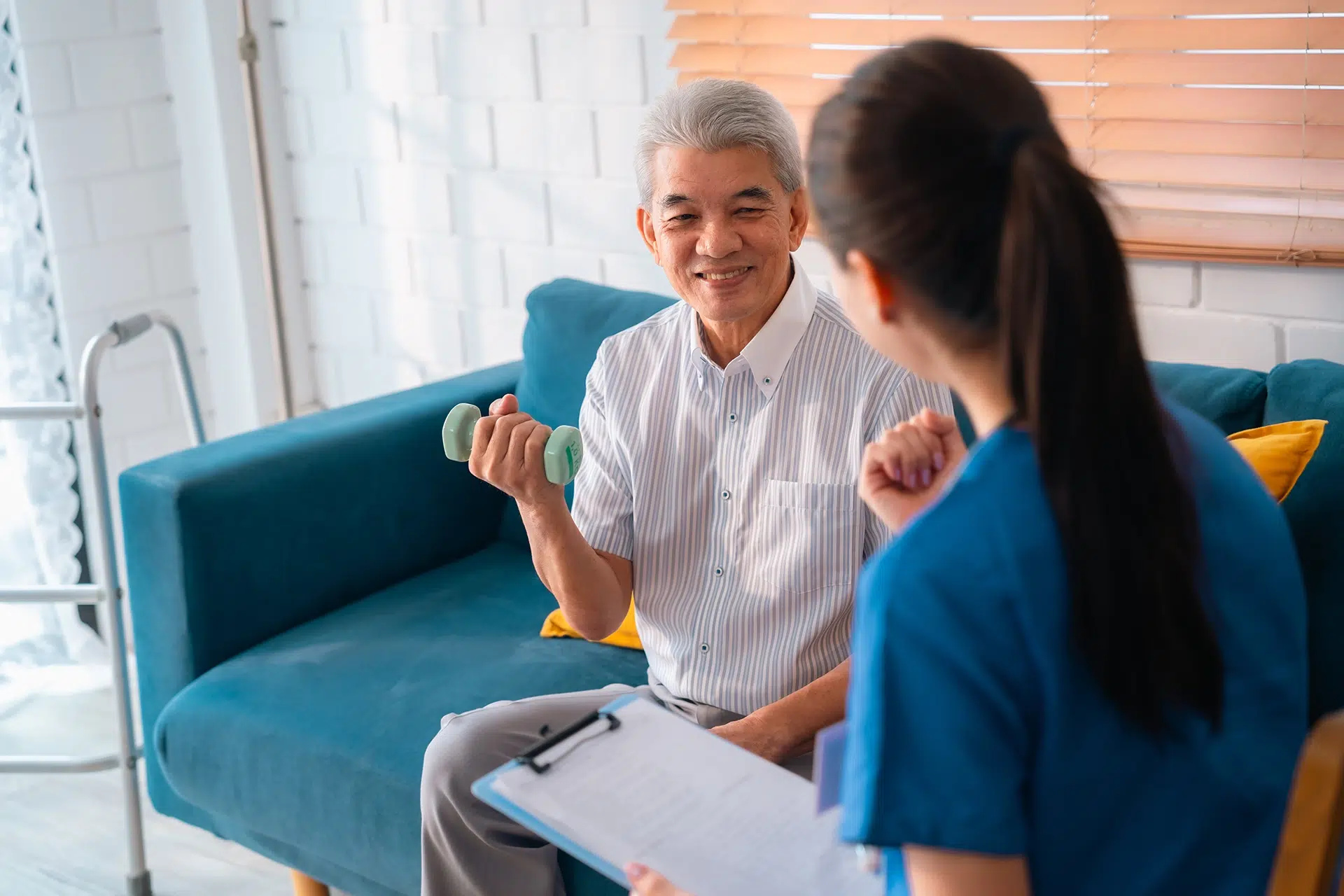 Senior man doing light exercise at home with support from a caregiver during a physical therapy session.